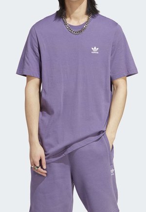 T-shirt en coton violet à manches courtes, avec un logo Adidas blanc sur la poitrine. Assorti à un short assorti et un collier en chaîne argentée.