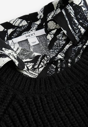 Maglione nero lavorato a maglia con un colletto a righe bianche e nere decorato con motivi floreali. Include un bottone decorativo sul colletto.