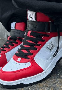 Kõrged spordijalatsid on valmistatud punasest ja valgest nahast ning mustade detailidega, mustad kengid, ja säärel on krooni logo.