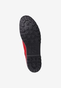 Roter Sneaker mit einer strukturierten schwarzen Gummisohle, die ein einzigartiges Profilmuster und Branding aufweist. Das Obermaterial ist strukturiert und kontrastiert mit der glatten Sohle.