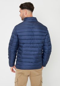 Giacca trapuntata blu navy con cuciture orizzontali, collo alto e una texture liscia e lucida. Design leggero e aderente per garantire calore.