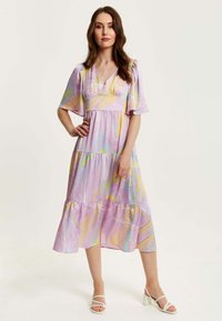 Maxi dress in lightweight fabric with pastel pink, yellow, and blue abstract patterns, featuring short flutter sleeves and tiered skirt.