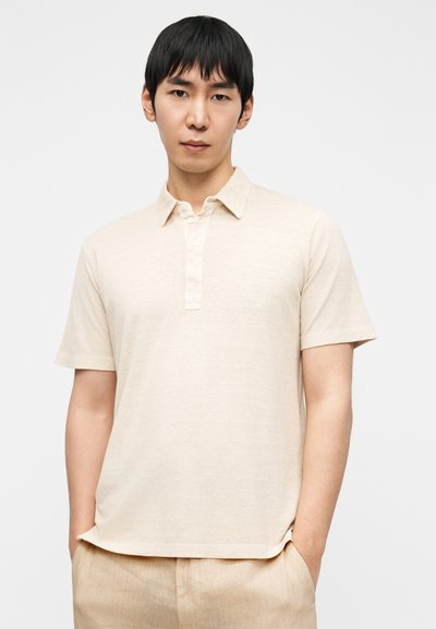 Ανοιχτό μπεζ πόλο μπλουζάκι με υφασμάτινη υφή, κοντά μανίκια και πλάκα με κουμπιά. Διαθέτει άνετη εφαρμογή και διακριτική λάμψη.