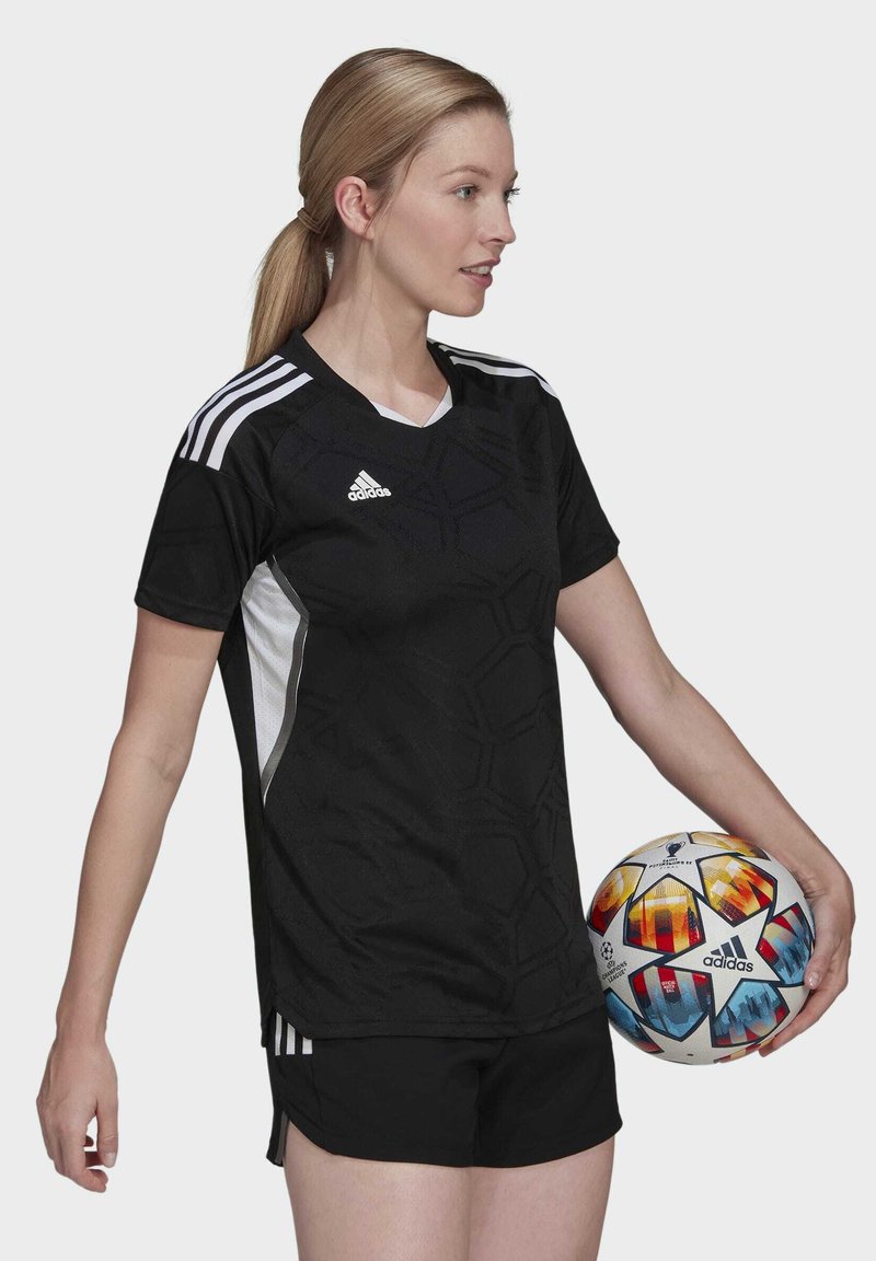 Camiseta atlética negra con textura hexagonal, acentos blancos, logo de Adidas; usada con pantalones cortos negros; sosteniendo un balón de fútbol multicolor.