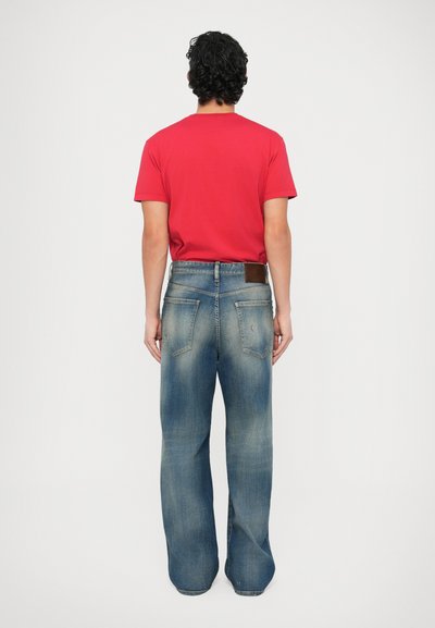 Červené tričko s krátkym rukávom v kombinácii s voľnými, svetlomodrými roztrhanými rifľami so zhnednutou koženou záplatou a zadnými vreckami.