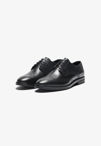 Chaussures habillées noires en cuir au fini lisse, à bout pointu, avec des perforations décoratives et un laçage. Talon en bois bas.