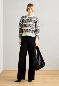Maglione a maglia con un motivo geometrico in bianco e nero, design corto e polsini a coste. Pantaloni neri a gamba larga e una borsa nera con texture.