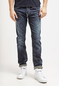 Mörkblå jeans i denim med en urtvättad look, slim fit och upplindade muddar. Kompletteras av vita höga sneakers. Synliga sömnadsdetaljer.