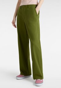 Gröna vida byxor i lätt tyg, med två framfickor och en avslappnad passform. Matchas med rosa sneakers.