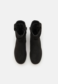 Bottes noires à hauteur de cheville avec un dessus doux et texturé, fermeture éclair sur les côtés et une doublure intérieure confortable. Détail de revers en haut.