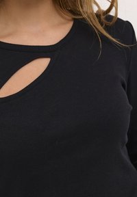 Maglia nera a maniche lunghe con coste, caratterizzata da un dettaglio cut-out sul collo, dalla silhouette aderente e dalla texture morbida.