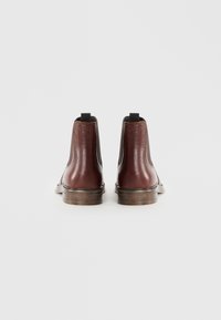 Bottines Chelsea en cuir marron avec une finition texturée, panneaux latéraux élastiques et languettes de tirage. Semelles en bois plates avec un léger talon.