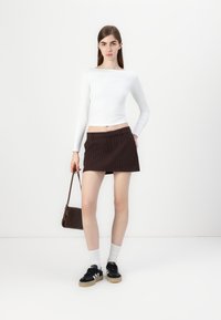 Fehér hosszú ujjú felső, barna csíkos mini szoknya, fekete sneakers fehér részletekkel, fehér zoknik és egy barna kézitáska.
