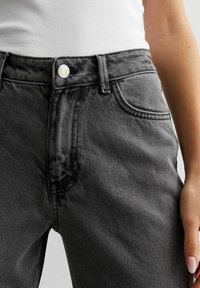 Černé džíny s vysokým pasem vyrobené z texturovaného denimu, s předním zapínáním na knoflík, dvěma bočními kapsami a jemnými švy.