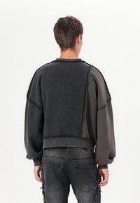 Sudadera de gran tamaño en color oscuro con un diseño de bloques de color, que presenta bordes deshilachados y un tejido texturizado. Mangas largas con hombros caídos.