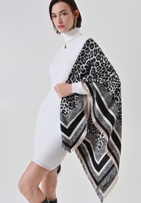 Écharpe à imprimé animal noir et blanc avec des franges, drapée sur une robe col roulé ajustée de couleur claire. Motif chevron audacieux le long des bords.
