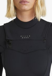 Black wetsuit with a high neckline and short sleeves. Features a zip closure, logo detail at the chest, and textured seams.