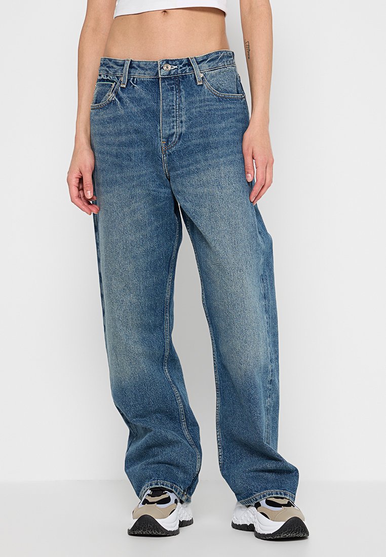 Szerokie niebieskie dżinsy z wysokim stanem, z zapięciem na guziki i przednimi kieszeniami, o wyblakłym wykończeniu i luźnym kroju.