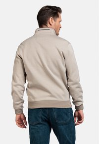 Lichtbeige sweatshirt met een hoge kraag, gestructureerde stof, ribbels aan de mouwen en een tailleband, gecombineerd met blauwe jeans. Achteraanzicht.