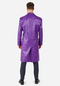Purple faux leather coat with a croc texture, long sleeves, straight cut, and back vent. Worn over dark textured trousers and black shoes.