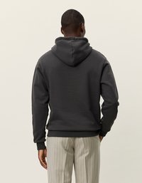 Dunkelgrauer Hoodie aus weichem Stoff, mit einer Kordelzugkapuze und gerippten Bündchen. Wird über hell gestreiften Hosen getragen und zeigt eine lockere Passform.