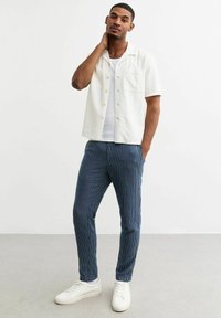 Witte kortemouwen shirt met knopen, lichte stof, gecombineerd met blauwe gestreepte broek en witte sneakers. Eenvoudige en casual outfit.
