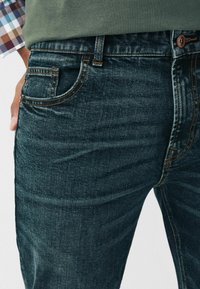 Jeansi din denim de un albastru închis, cu croială slim, prezentând cusături portocalii contrastante, un buzunar frontal și o închidere cu nasture la talie.