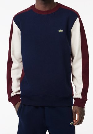Sudadera azul marino con mangas blancas y granate. Presenta puños acanalados, cuello redondo y un pequeño logotipo verde en el pecho. Material de mezcla de algodón.