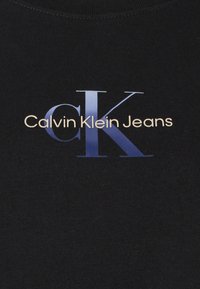 Czarna bawełniana koszulka z dużym, gradientowym niebieskim logo "CK" oraz napisem "Calvin Klein Jeans" białą czcionką poniżej. Klasyczny krój z okrągłym dekoltem.