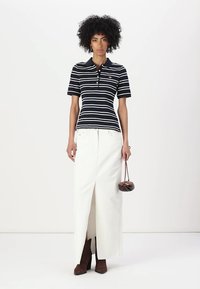 Polo shirt bleu marine à rayures, à manches courtes et avec col. Jupe maxi blanche avec une fente à l'avant. Bottes à talons marron et petit sac à main marron.