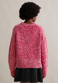 Roter und weißer gestrickter Pullover mit lockerer Passform, geripptem Saum und Raglanärmeln, strukturiertem Muster, von hinten gezeigt.