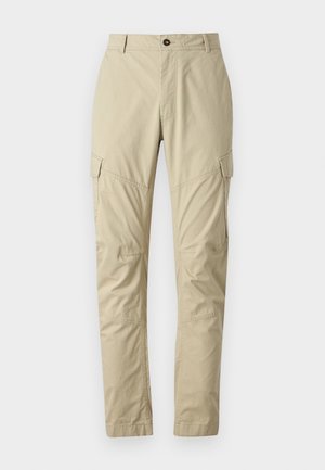 Beige sääret, mis on valmistatud kergest kangast, sisaldavad mitmeid taskuid, nuppe sulgemiseks ja kitsenevat säärejoont. Sile tekstuur.