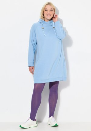 Abito felpa azzurro chiaro con collo a cowl, tasca laterale e dettaglio con cordino. Abbinato a collant viola e sneakers bianche.