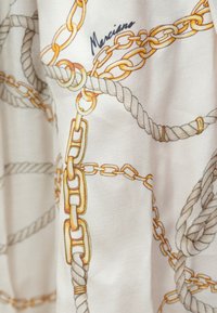 Gai audums ar ieaustām dzeltenām ķēdēm un pelēkām virvēm uz krēmkrāsas fona. Vārds "Marciano" ir neticami nospiests.