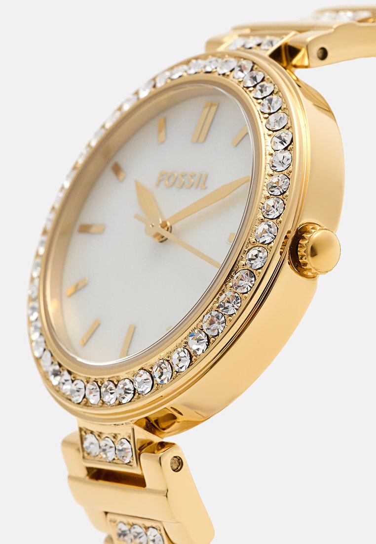 Gouden polshorloge met een witte wijzerplaat, een bezel versierd met kristallen, gouden uur-markeringen en een schakelarmband ontwerp.