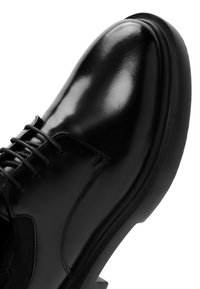 Glanzend zwart leren broekschuh met ronde neus, zwarte veters en stevige rubberen zool, gezien vanuit een close-up hoek.