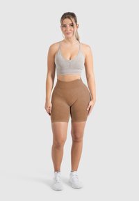 Scollo a V e spalline sottili, il reggiseno sportivo grigio chiaro è abbinato a pantaloni corti marroni a vita alta. Le scarpe da ginnastica bianche completano il look.