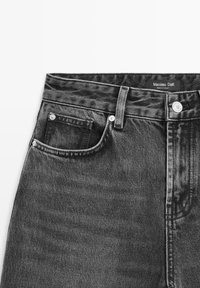 Zone de la taille d'un jean en denim noir avec poche avant, passants de ceinture, bouton métallique et étiquette indiquant « Massimo Dutti Made in Turkey ». 