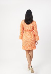 Orangenes Blumenkleid mit langen Ärmeln, tailliertem Schnitt und rüschenförmigem Saum. Es besteht aus einem leichten Stoff und hat kleine weiße Blumenmuster.