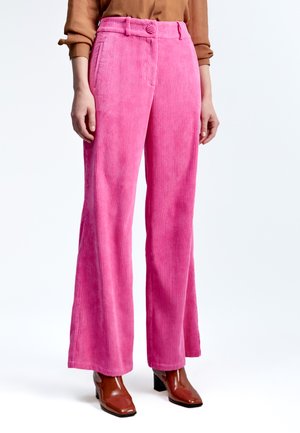 Pantalones de pana anchos de color rosa con acanalado vertical, cintura con cinturón y bolsillos laterales. Combinados con botas de tobillo de tacón marrones.
