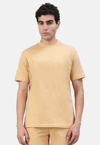 T-Shirt mit kurzen Ärmeln und rundem Ausschnitt in einem hellbeigen Farbton. Hergestellt aus weichem Stoff mit glatter Textur, zeichnet sich durch schlichte Linien und einen lässigen Schnitt aus.