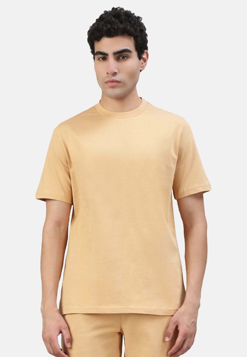 T-Shirt mit kurzen Ärmeln und rundem Ausschnitt in einem hellbeigen Farbton. Hergestellt aus weichem Stoff mit glatter Textur, zeichnet sich durch schlichte Linien und einen lässigen Schnitt aus.