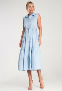 Jasnoniebieska sukienka bez rękawów z kołnierzykiem, z przodu na guziki oraz wiązaniem w talii. Posiada warstwową spódnicę i gładką fakturę materiału.