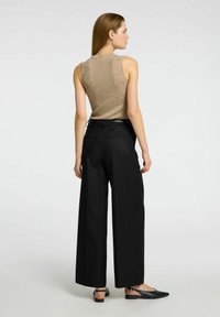 Beige ribbet tanktop uden ærmer, parret med høj Talje, sorte vide bukser og sorte slingback sko, set fra ryggen.