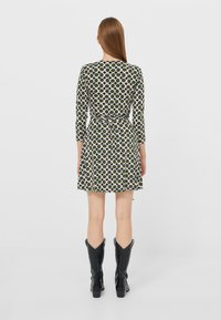 Grünes Kleid mit großen pinken und weißen Kreisen, 3/4-Ärmel, tailliert, schwingender Rock, strukturiertem Material, kombiniert mit schwarzen Cowboystiefeln.