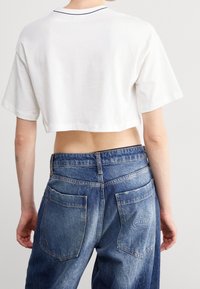 Vit kortärmad t-shirt med en klassisk halsringning, tillsammans med blå högmidjade jeans i denim som har fickor med lappar och urblekta områden.