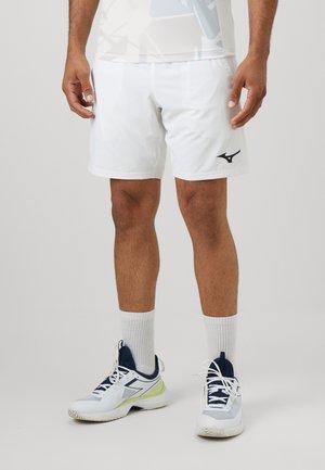 Vitaid atletiska shorts med en svart logotyp på vänster ben, kombinerat med vita strumpor och vit-blå atletiska skor med gröna detaljer.