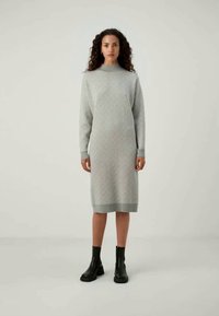 Vestido de malha em cinza claro com um padrão zigzag texturizado, mangas longas e um decote alto. Combinado com botas de tornozelo pretas.