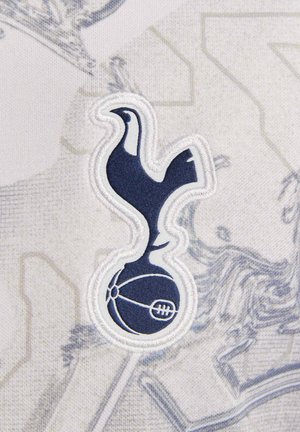 Logo ricamato blu marina di un gallo all'interno di un emblema circolare su uno sfondo grigio chiaro con un motivo sottile.