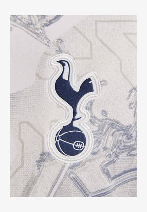 Marineblauw geborduurd logo van een haan binnen een cirkelvormig embleem op een lichtgrijze achtergrond met een subtiel patroon.